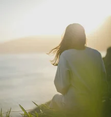 Person sitting by the sea looking toward the horizon.
