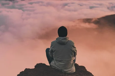 Person sitting on a mountain above the clouds.
