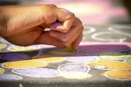 Hand creating colorful chalk drawings on pavement.