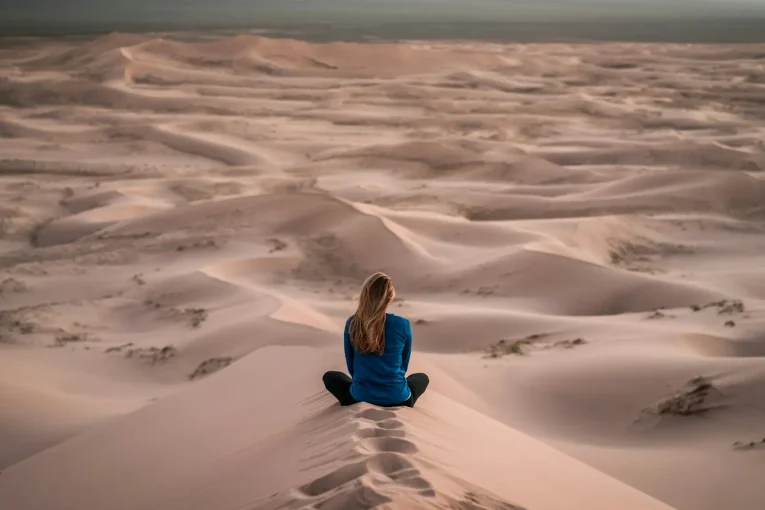 Person sitting alone among rolling sand dunes.