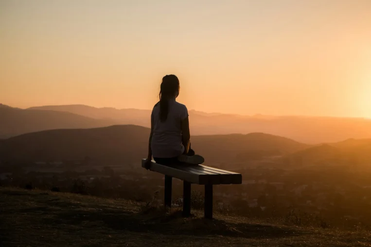 Person meditating on a bench at sunset.