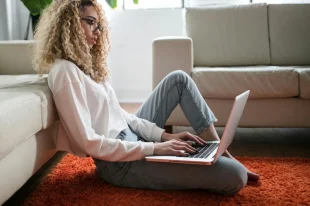 Woman working on a laptop while sitting on the floor.